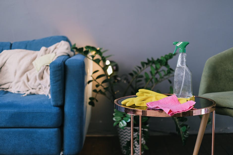 A professional cleaner from Tenancy Cleaning, dressed in white protective coveralls and orange gloves, is operating a yellow vacuum cleaner on a light grey tiled living room floor. The room features a